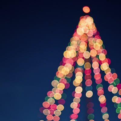 Colorful bokeh lights forming a Christmas tree against a dark blue sky.