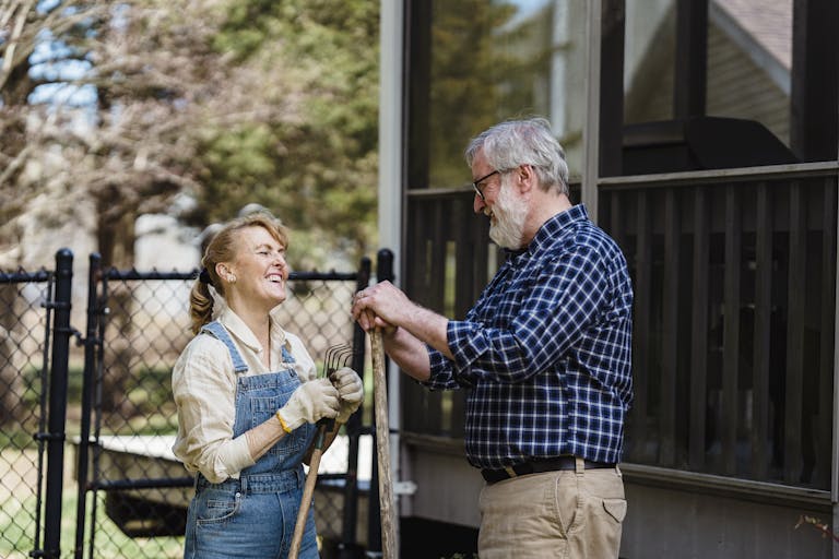 Elderly couple enjoying gardening in their backyard on a sunny day, filled with smiles and joy.