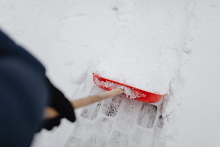 A person shoveling snow with a red shovel on a snowy day outdoors.