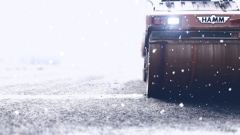 Close-up of a road roller working on an icy highway during heavy snowfall.