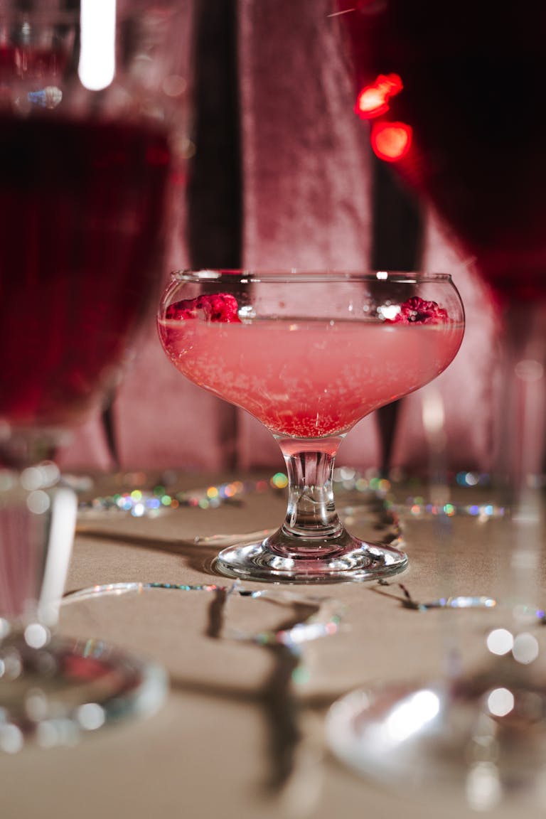 Close-up of a pink cocktail with raspberries in an elegant glass on a festive table.