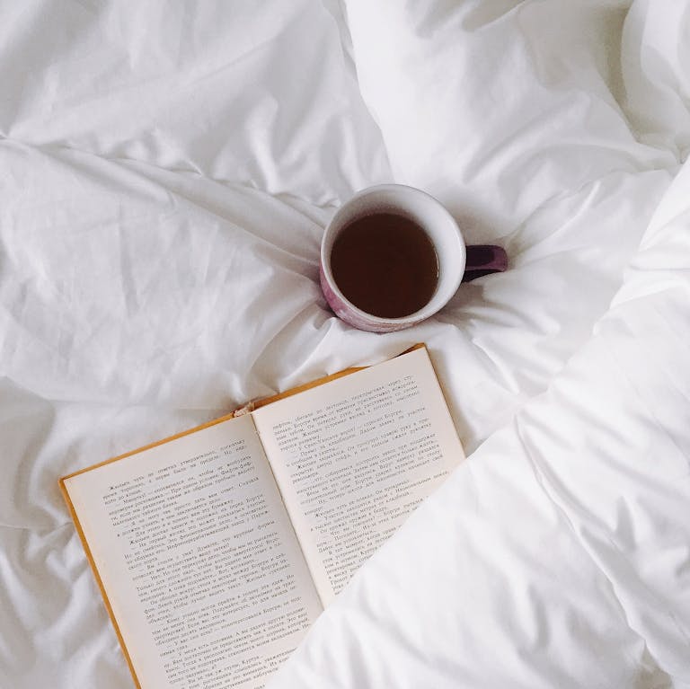 An inviting setup with a warm cup of tea and open book on white bedding, ideal for relaxation.