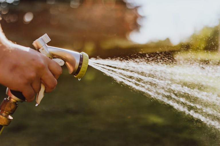 Close-up of a hand holding a garden hose, spraying water outdoors on a sunny day.